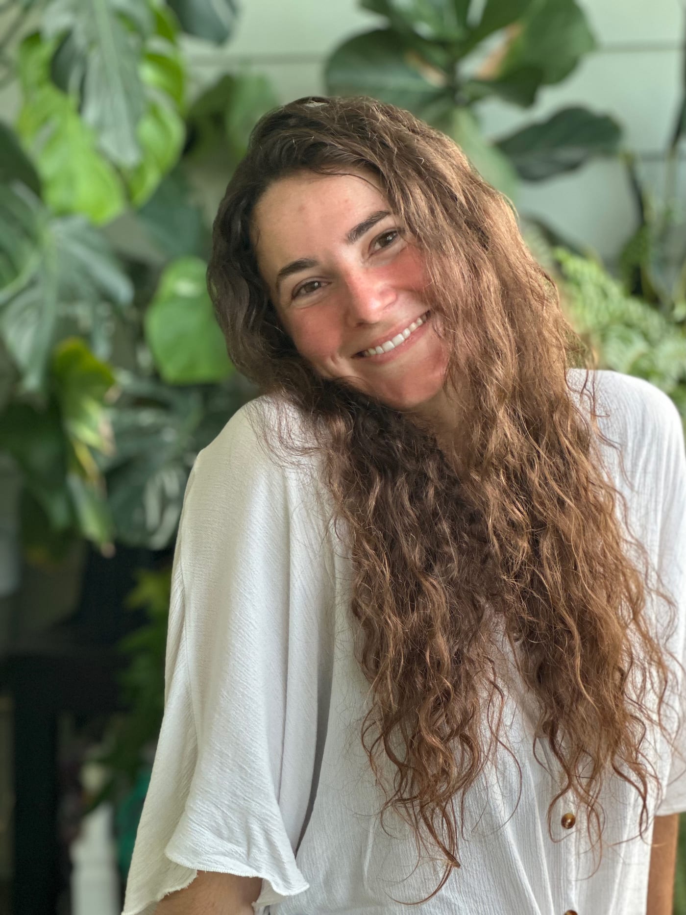 Jaci Brumble, smiling, in front of a wall of houseplants including a monstera and a fiddle-leaf fig